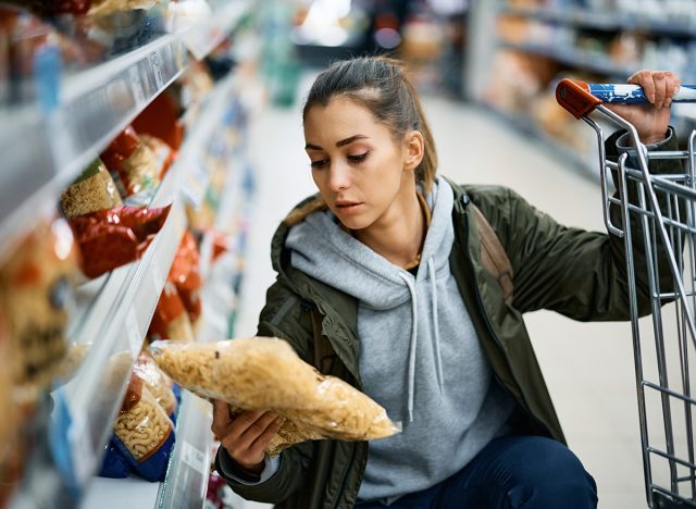 Young woman label on pasta package while shopping food in supermarket.