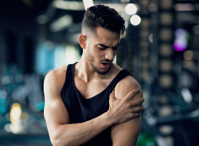 Portrait Of Young Arab Man With Shoulder Pain Suffering Sport Injury During Training At Gym, Middle Eastern Male Athlete Having Trauma After Fitness Workout, Rubbing Painful Area, Closeup