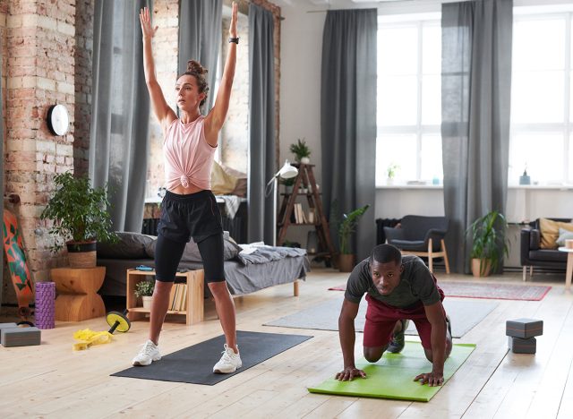 Horizontal wide shot of sporty young man and woman exercising in morning in loft living room at home