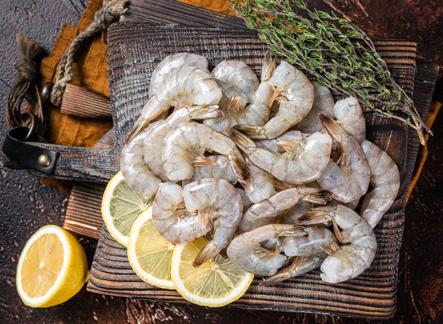 Raw tiger white shrimp prawn on board with herbs. Dark background. Top view.