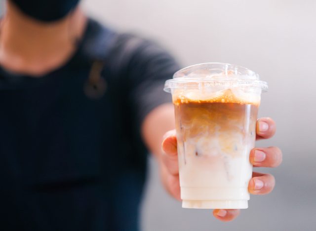 Cold brewed iced latte coffee, Ice coffee latte cup in a plastic glass on. barista hand in coffee cafe.banner background.Cold brew coffee ads.Latte with milk caffeine.plastic ice cup.Arabica roasted.