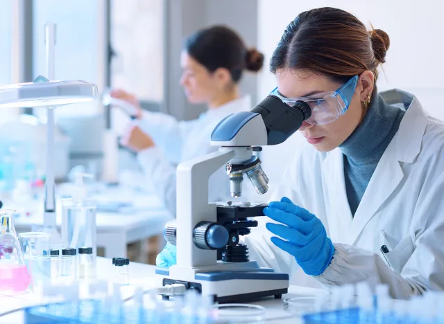 Young scientists conducting research investigations in a medical laboratory, a researcher in the foreground is using a microscope