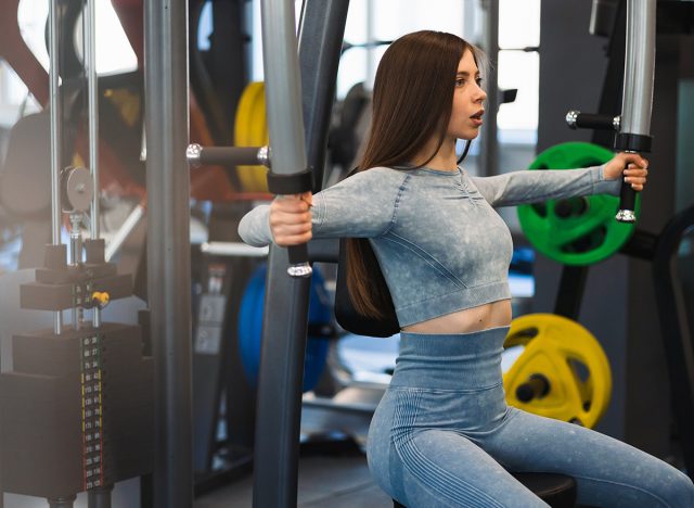 Caucasian young fitness woman is working out on butterfly machine in gym