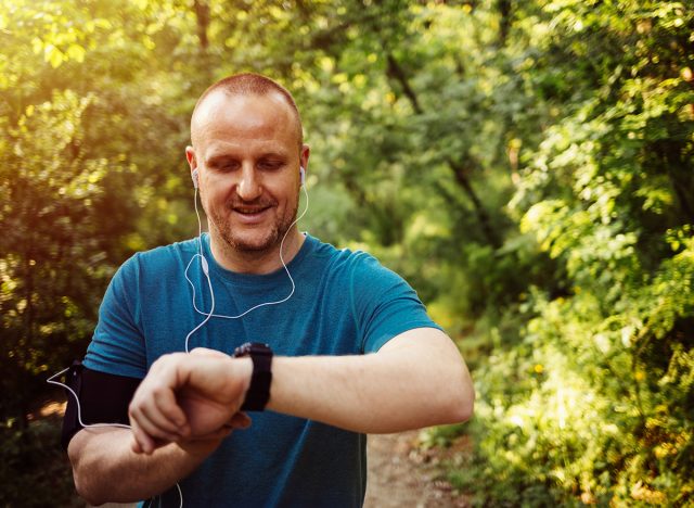 Young Caucasian men using Smart Watch measuring heart rate during walk. Runner fixing time at sports smart watch. Young athletic man using fitness tracker or smart watch before run training outdoors.