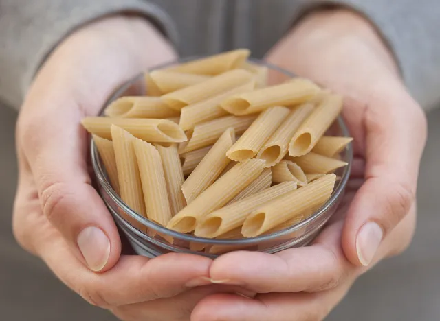 Organic brown rice pasta penne in a bowl in woman's hands. (Gluten Free Product).