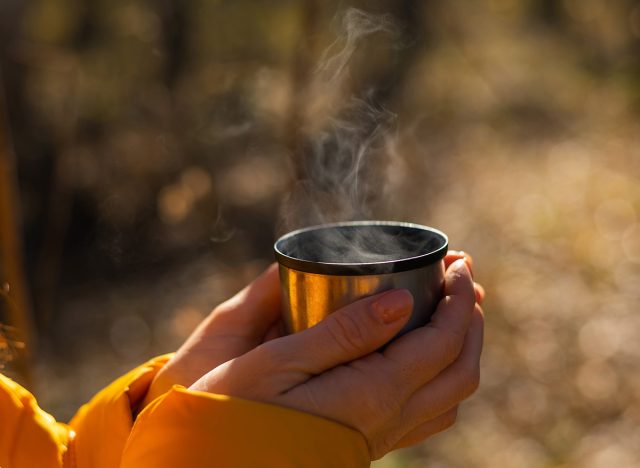 A woman holds a thermos of hot tea in her hands on a cold autumn day.