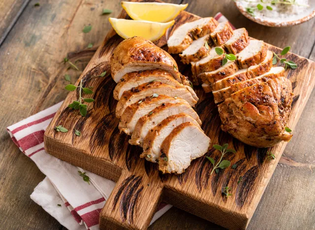 Roasted or seared chicken breast sliced on a cutting board with herbs and spices