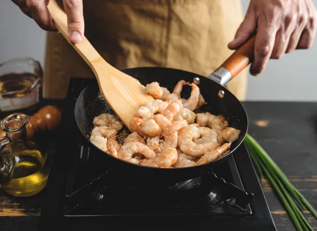 Cook hands cooking big tiger shrimps and frying on wok pan, close up steps recipe on kitchen background