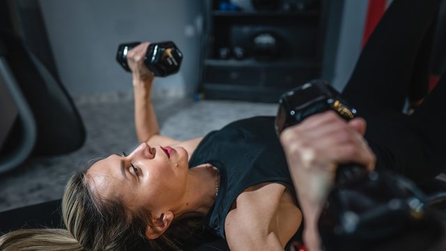 One woman mature caucasian female slim hands hold dumbbell while training at home or fitness center real people healthy lifestyle concept copy space