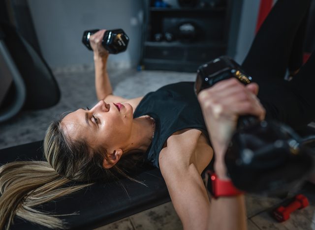 One woman mature caucasian female slim hands hold dumbbell while training at home or fitness center real people healthy lifestyle concept copy space