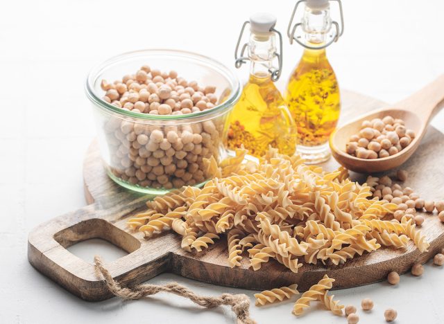 Chickpea bean fusilli pasta on a gray concrete background. Bowl with raw pasta and chickpea bean. Gluten free pasta.