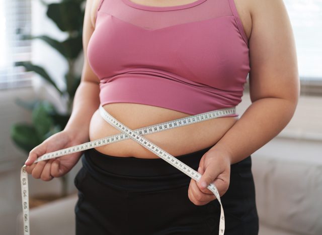 Close up overweight woman measuring her hip with tape measure.