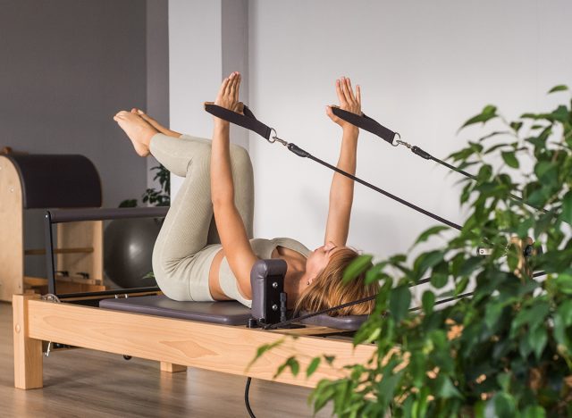 Woman training pilates on the reformer bed. Reformer pilates studio machine for fitness workouts in gym. Fit, healthy and strong authentical body. Fitness concept