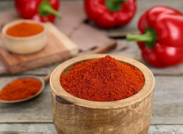 Bowl with aromatic paprika powder on wooden table, closeup