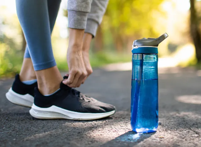 Drinking water and staying hydrated. Person running in the park trying shoe next to bottle of water.