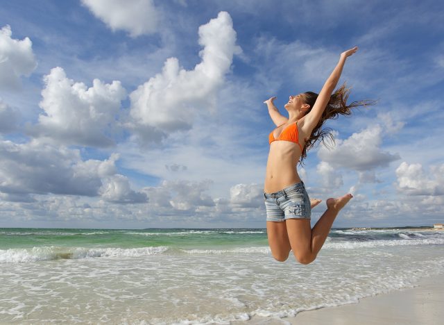 Happy girl wearing bikini jumping on the beach on holidays with a cloudy sky in the background