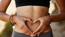 Woman, stomach and hand with heart in outdoor for exercise, diet, fitness and closeup. Female tummy, gut health and self love for wellness and training in the summer for healthy workout outside.