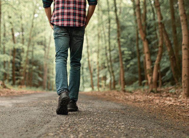 Man walking on sunlit trail in autumn forest enjoying peaceful walk in nature