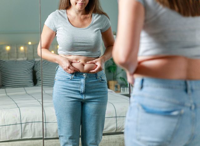 Young woman touching her belly looking in mirror at home