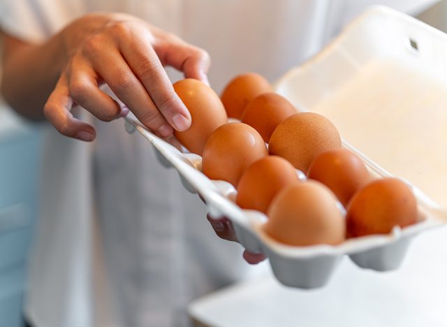 women with holding a cardboard egg box full of her eggs. the girl takes one chicken egg from a white box