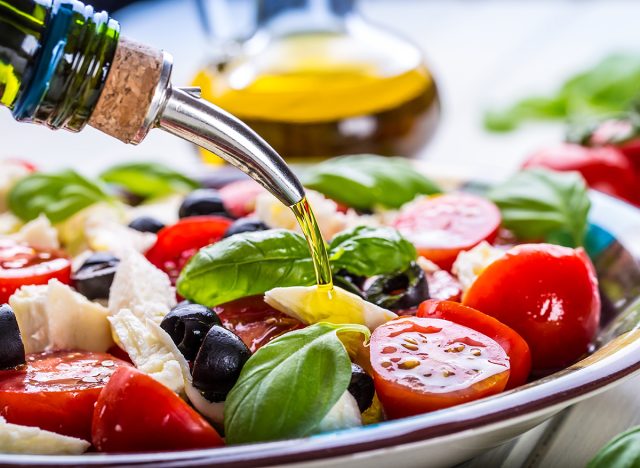 Caprese Italian or Mediterranean salad. Tomato mozzarella basil leaves black olives and olive oil on wooden table.