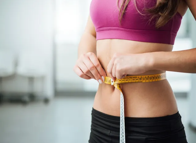 Slim young woman measuring her thin waist with a tape measure, close up