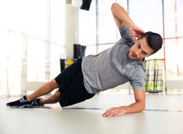 Portrait of a handsome man doing side plank at gym