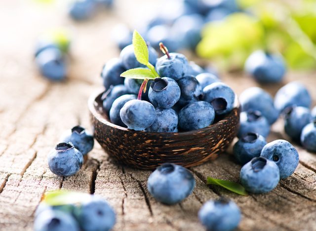 Freshly picked blueberries in wooden bowl. Juicy and fresh blueberries with green leaves on rustic table. Bilberry on wooden Background. Blueberry antioxidant. Concept for healthy eating and nutrition