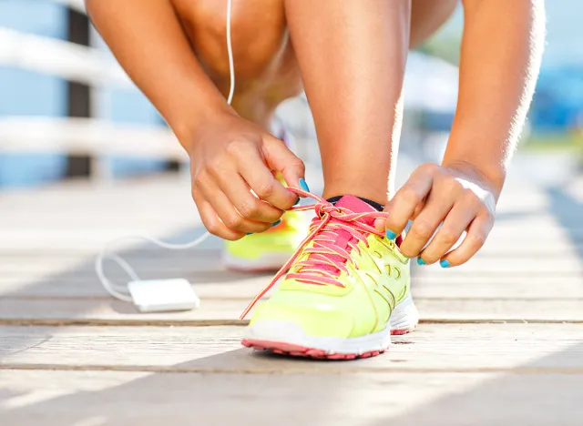 Running shoes - woman tying shoe laces. Closeup of female sport fitness runner getting ready for jogging outdoors on waterfront in late summer or fall