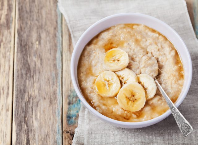 Bowl of oatmeal porridge with banana and caramel sauce on rustic table, hot and healthy breakfast every day, diet food.