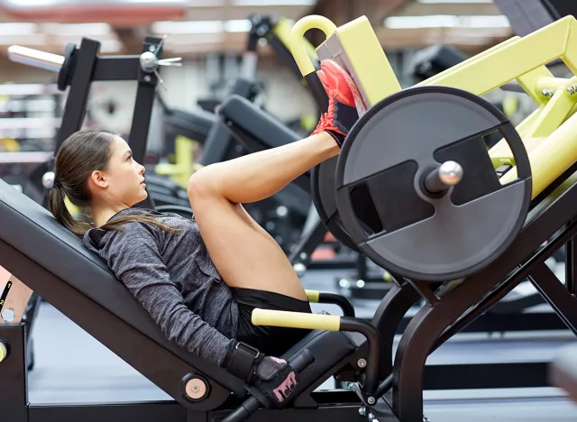 woman flexing muscles on leg press machine in gym