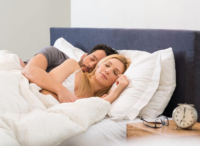 Young adult couple sleeping peacefully on the bed in bedroom. Young man embracing woman while lying asleep. Loving couple sleeping lying in bed at home.