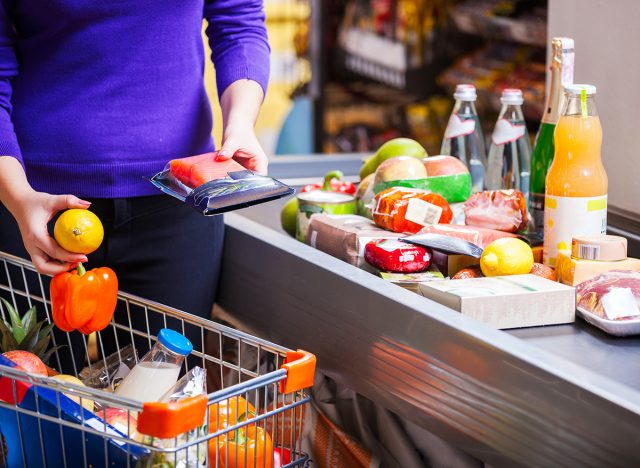 Young woman putting goods on counter in supermarket