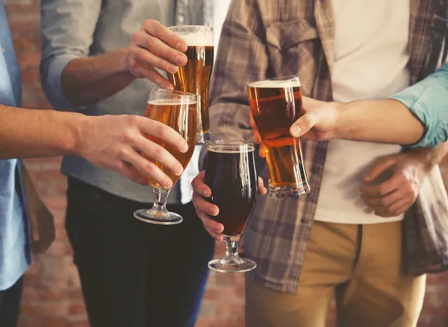 Male group clinking glasses of dark and light beer on brick wall background
