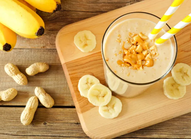 Peanut butter banana oat smoothie with paper straws, on a wood board on rustic table, downward view