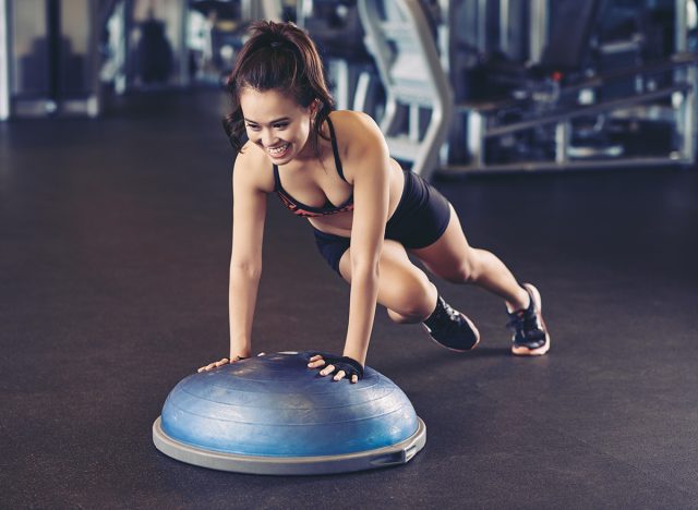 Cheerful Asian woman training with bosu ball