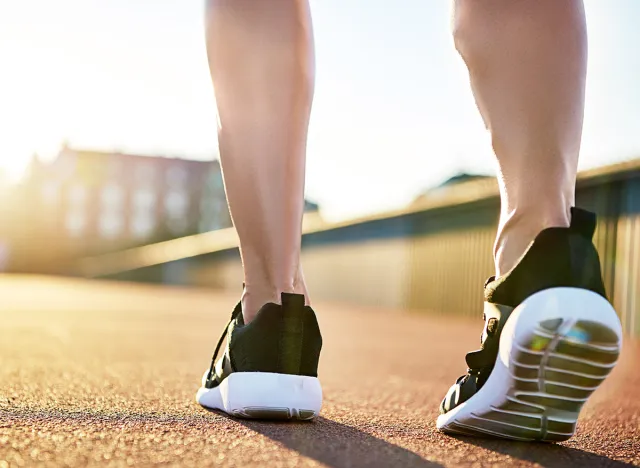 Bare legs in running shoes preparing to exercise on a bright summer day on an empty road