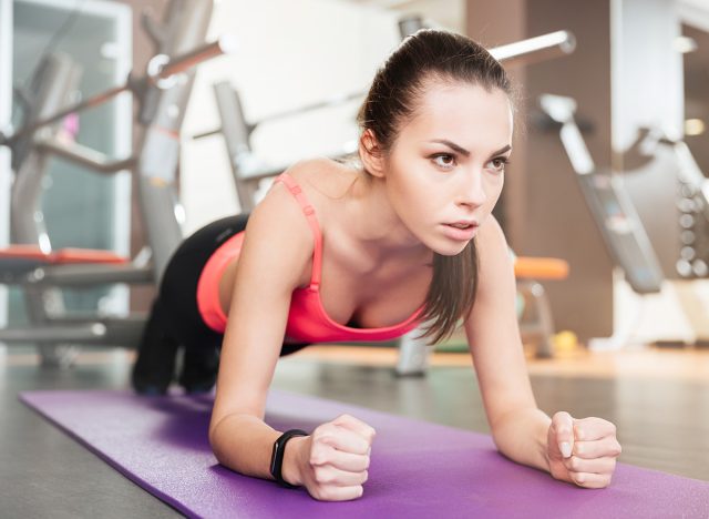 Concentrated beautiful young sportswoman doing plank exercise on mat in gym