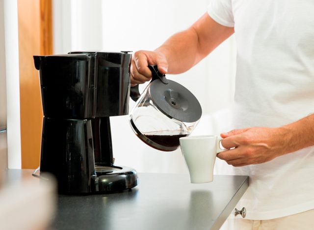 Man in the kitchen pouring a mug of hot filtered coffee from a glass pot. Having breakfast in the morning