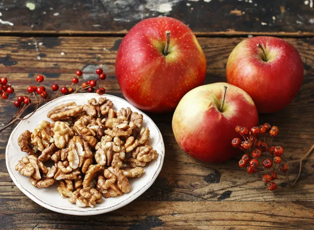 Bowl of walnuts and red apples on wooden table. Healthy snacks.