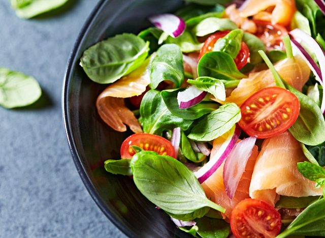 Salmon Salad with spinach, cherry tomatoes, corn salad, baby spinach, fresh mint and basil. Home made food. Concept for a tasty and healthy meal. Dark stone background. Top view. Close up.