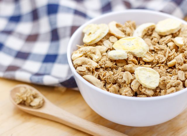 Healthy breakfast, granola with nuts and dry bananas in white blow on wooden table with wooden spoon and cute fabric.