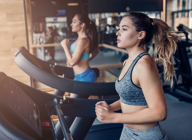 Side view of two attractive sports women on running track. Girls on treadmill