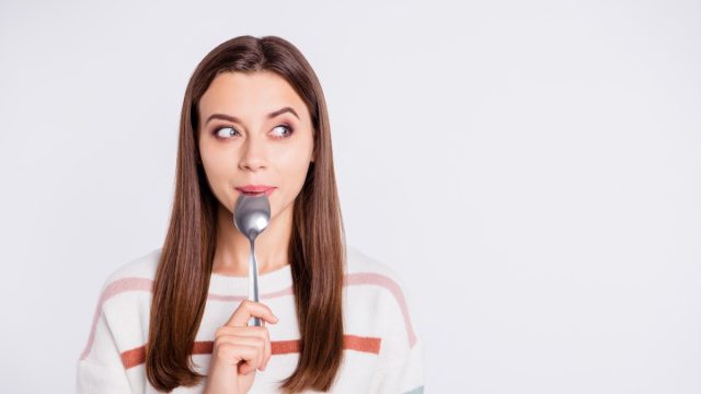 Hungry woman holding spoon in her mouth.