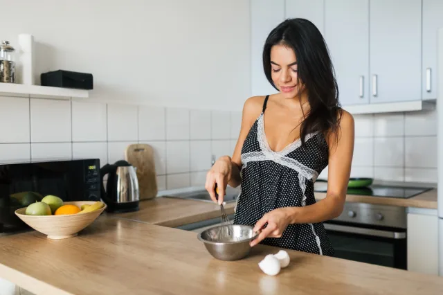 attractive young skinny smiling woman having fun cooking eggs at kitchen in morning having breakfast dressed in sexy pajamas outfit