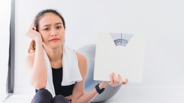Asian woman satisfied with holding bathroom scales on white background.
