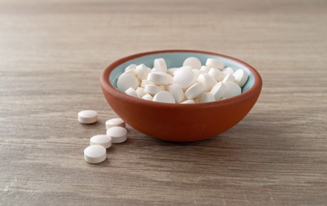 Side view of several DHEA pills in a small bowl and on a tile table top illuminated with natural lighting.
