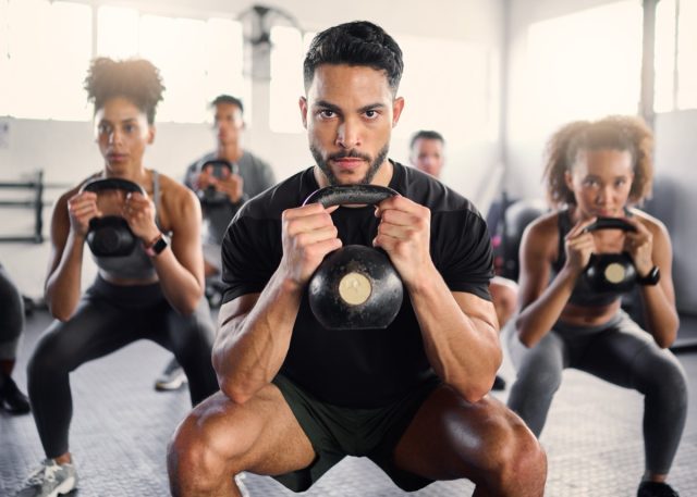 Kettlebell, workout and fitness class with a gym coach and people training with cardio and exercise. Portrait of a strong personal trainer and sports friends in a wellness health club with motivation