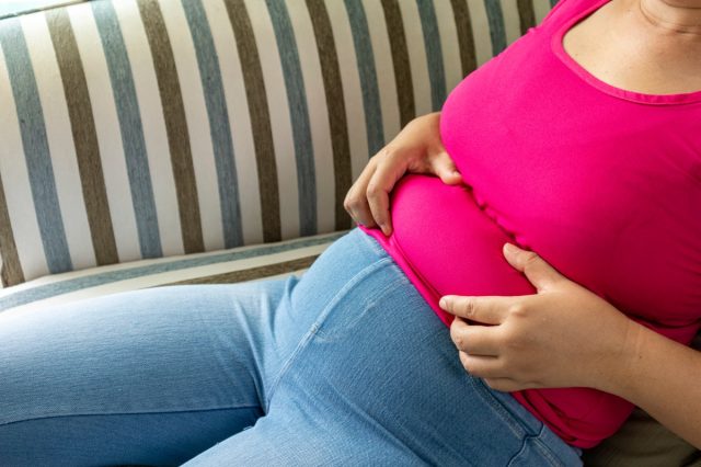 Asian fat women wear pink t shirt . She has overweight and she shows excess fat of the waist. She sit on her sofa and wants lose weight. concept of surgery and subcutaneous fat breakdown.