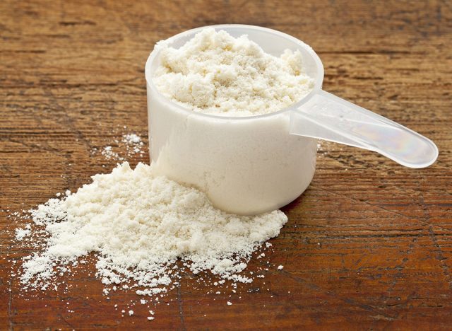 plastic measuring scoop of white powder (whey protein) against grunge wood background